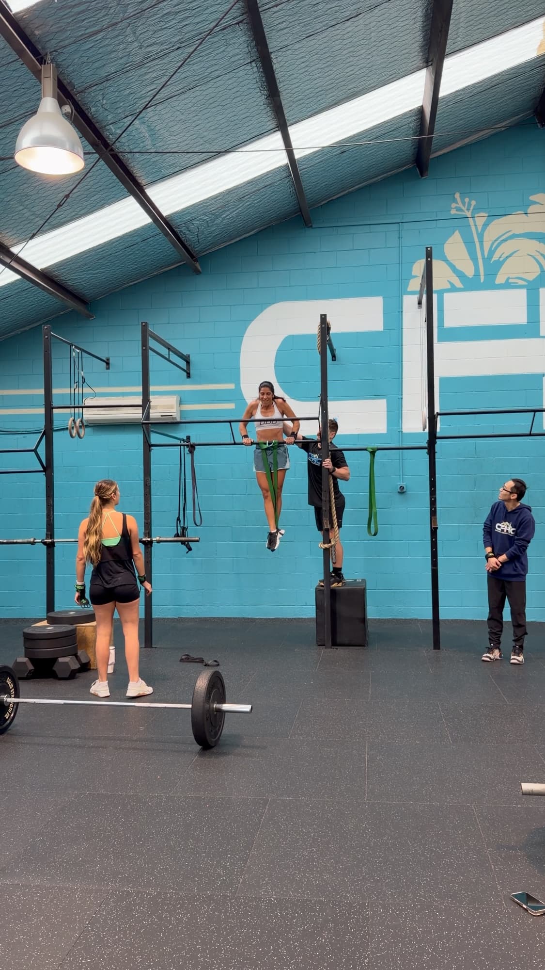 An athlete doing pull-ups on the rig while Coach Julz Halkyard helps from a box at CrossFit Hibiscus Coast