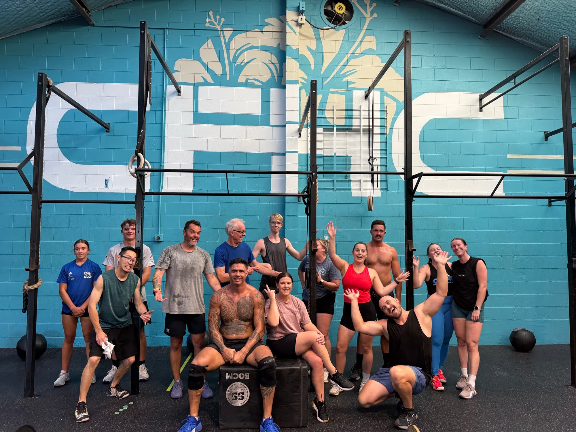 CrossFit Hibiscus Coast athletes gathered together in front of the gym mural wall